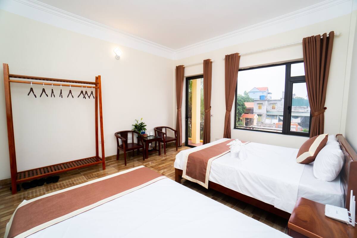 Une chambre d’hôtel avec deux lits, une chaise en bois, une petite table et une fenêtre avec des rideaux.