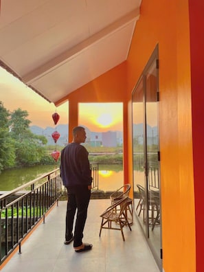 Een man staat op een balkon met uitzicht op een rivier en bergen in de zonsondergang.
