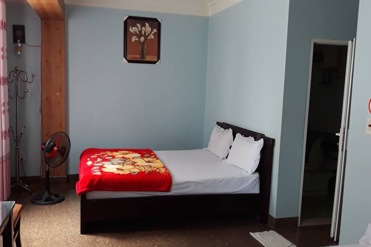 Ein Schlafzimmer mit einem Bett, einem Ventilator, einem Vorhang und einem Wandbild.