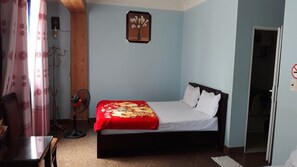 A bedroom with a bed, a fan, a curtain, and a wall-mounted picture. - Kim Thoa Motel (Hai Phong)