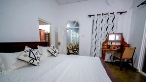 A hotel room with a large bed, a wooden desk with a chair, a mirror, and a view of a hallway. - Lagoon Bay Negombo (Negombo)