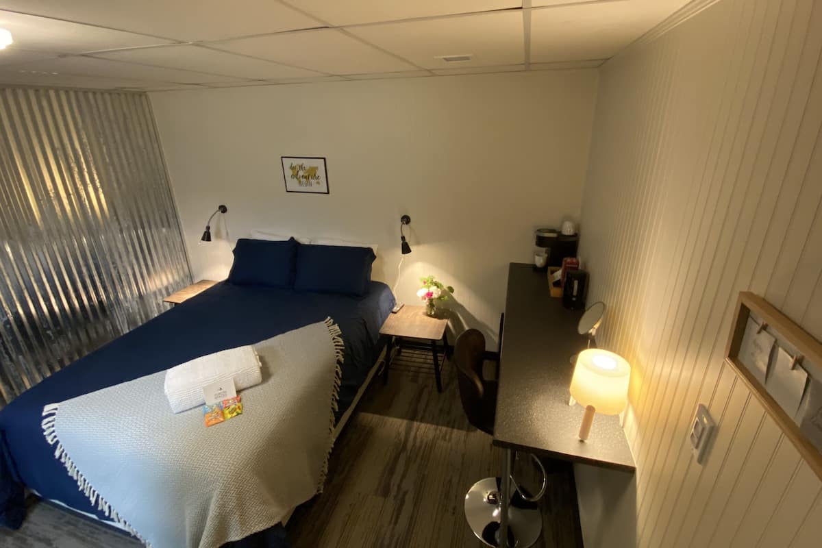 A hotel room with a bed, bedside table, desk, chair, lamp, and a mirror.