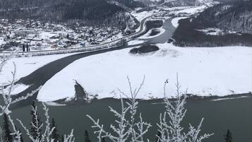 Paisagem coberta de neve com um rio, uma cidade e montanhas ao fundo.