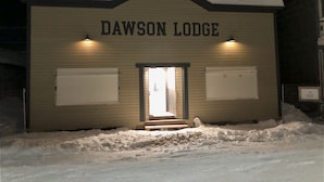 A building labeled "DAWSON LODGE" with a snow-covered entrance and two lit windows. - Dawson Lodge (Dawson City)