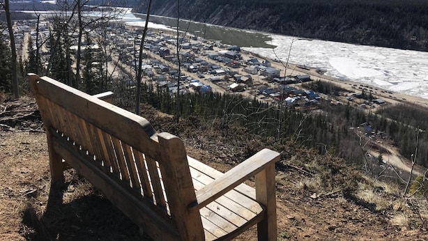 A wooden bench overlooking a river with a town in the valley below. - Dawson Lodge (Dawson City)