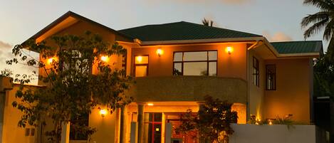 A two-story house with a balcony, a motorcycle parked in front, and a well-lit entrance.
