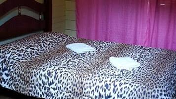 Una cama con cubrecama estampado de leopardo y dos almohadas, cabecera de madera y alfombra con motivos en el suelo.