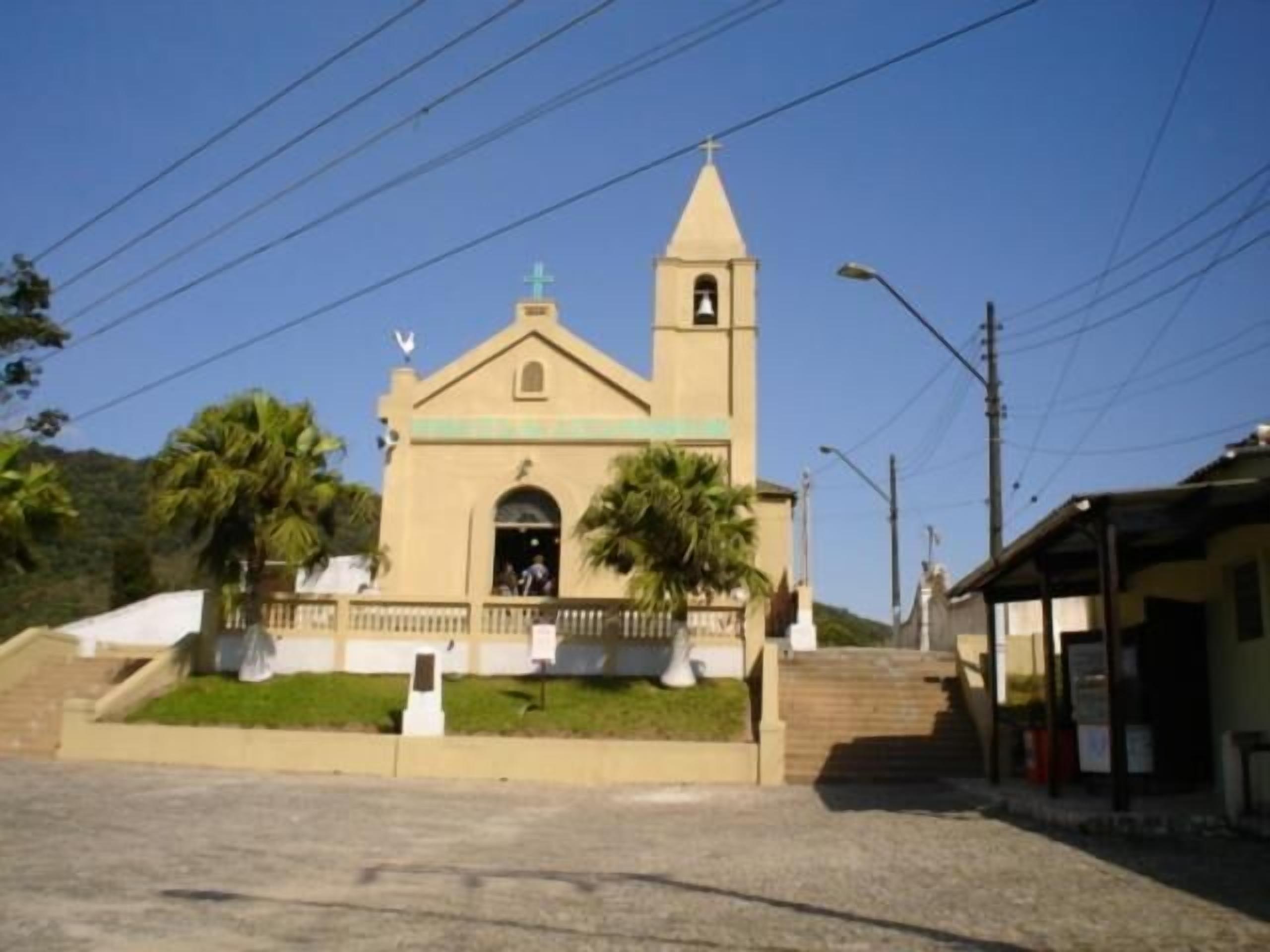 A church with a bell tower and a cross on top, surrounded by palm trees and a clear sky.