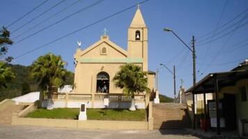 A church with a bell tower and a cross on top, surrounded by palm trees and a clear sky.