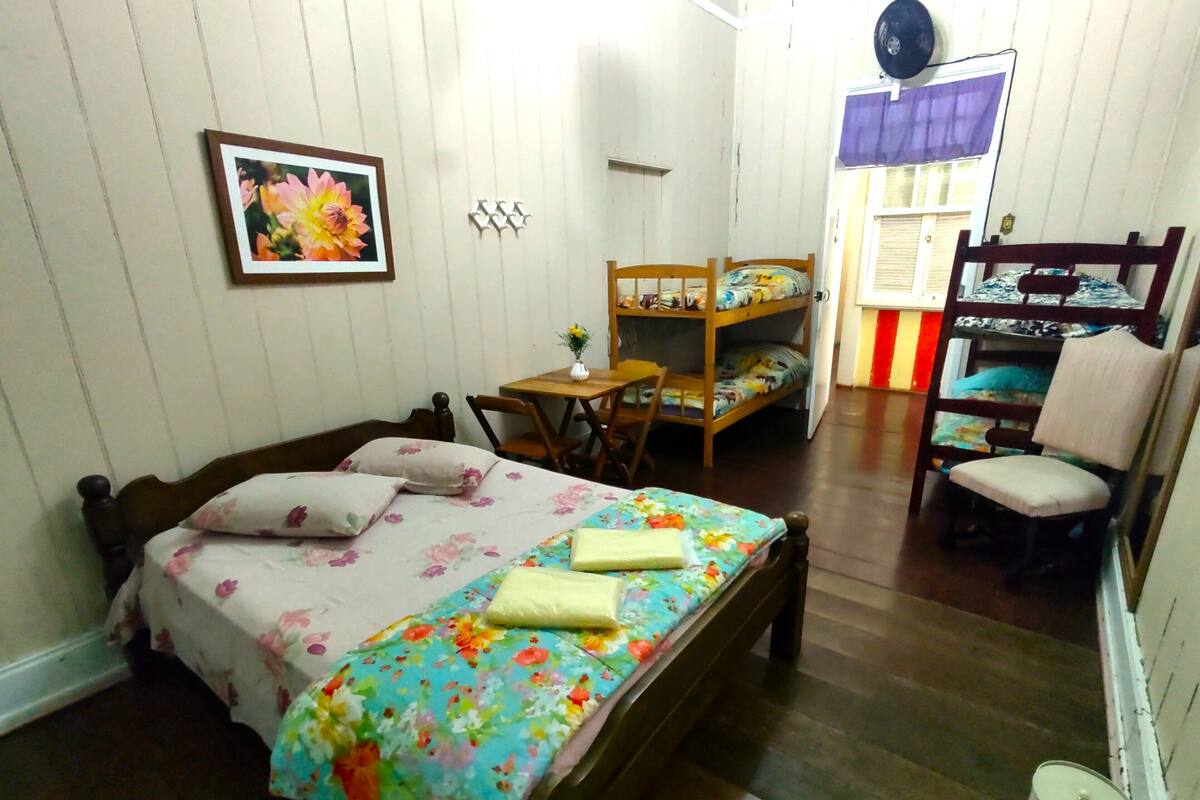A bedroom with a wooden bed, a small table with a vase, and a bunk bed in the background.