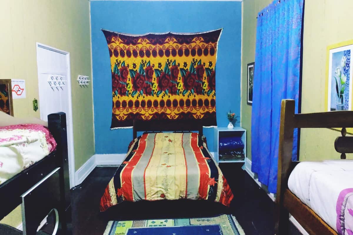 A room with a bed, a chair, a small table, a tapestry, and a blue curtain.