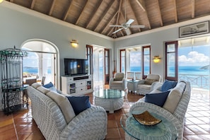 A spacious living area with wicker furniture, a glass coffee table, and a television.