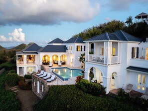A large house with a swimming pool, multiple balconies, and a view of the surrounding landscape.