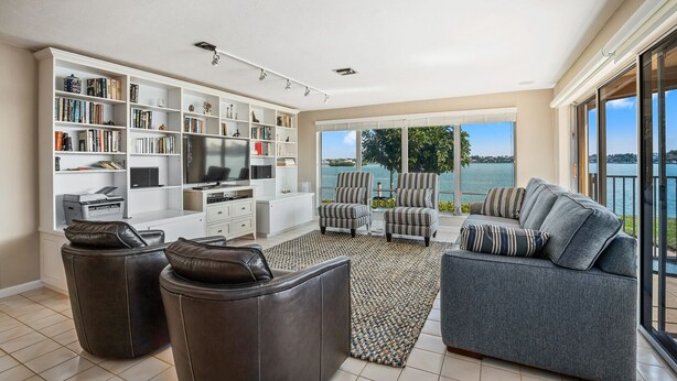 Ein geräumiges Wohnzimmer mit einer großen Bücherwand, einem Flachbildfernseher und einem Sofa, das einen Balkon mit Blick auf das Wasser überblickt.