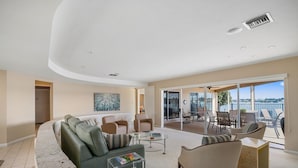 A modern living room with a curved ceiling, a sofa, armchairs, a coffee table, and a view of the outdoors through large sliding glass doors.
