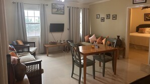 A living room with a dining table, chairs, a sofa, a TV mounted on the wall, and a ceiling fan. - Comfy and Secure  One Bedroom Apt- Sleeps 3!! (New Kingston)