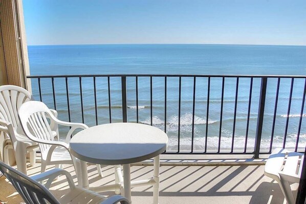 A balcony with a view of the ocean, white plastic chairs, and a small round table.