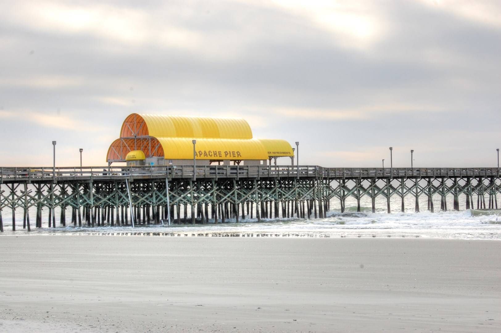 Historic Apache Pier stretches into the Atlantic Ocean with distinctive yellow buildings marking this iconic Myrtle Beach landmark.