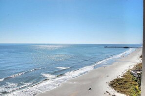 A beach with a pier extending into the water, a clear sky, and a few people on the sand.