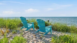 Two Adirondack chairs on a sandy beach with a view of the ocean.