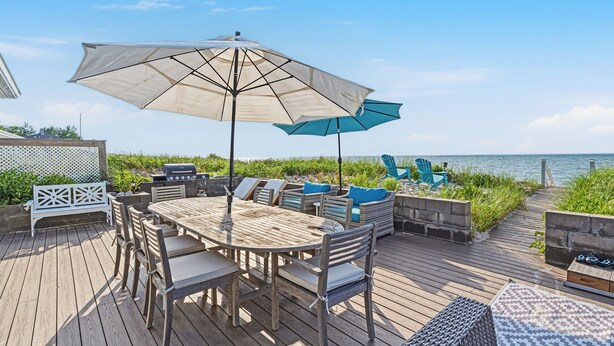 A wooden deck with a table and chairs, a large umbrella, and a view of the ocean.
