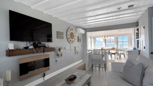 A living room with a large flat-screen TV, wooden shelves, a fireplace, a dining area with a view, and a white ceiling.