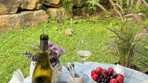 A table set outdoors with a bottle of wine, a glass, a plate of sushi, and a bowl of fruit. - St-Sauveur Lovely King Studio (Piedmont)