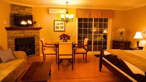 A hotel room with a fireplace, a TV, a dining table with chairs, a bed, and a nightstand with a lamp. - St-Sauveur Lovely King Studio (Piedmont)