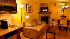 A cozy living room with a sofa, coffee table, and fireplace. There is a kitchen area with a microwave and coffee maker. - St-Sauveur Lovely King Studio (Piedmont)