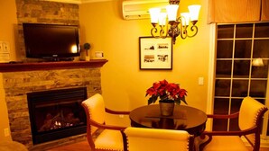 A living room with a fireplace, a television, a chandelier, and a dining table with chairs. - St-Sauveur Lovely King Studio (Piedmont)