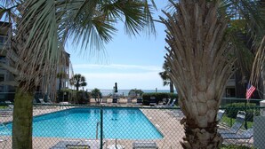 A swimming pool surrounded by palm trees and lounge chairs, with a view of the ocean in the background. - Popular Golden Mile location within a short distance to many local attractions! (Myrtle Beach)