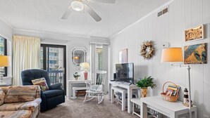 A cozy living room with a ceiling fan, a TV, a white rocking chair, a blue armchair, and a bookshelf. - Popular Golden Mile location within a short distance to many local attractions! (Myrtle Beach)