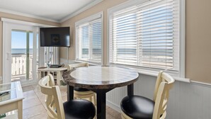 A sunlit room with a round table, two chairs, a television, and large windows with blinds. - Outstanding ocean front views in fabulous beach condo location! (Myrtle Beach)