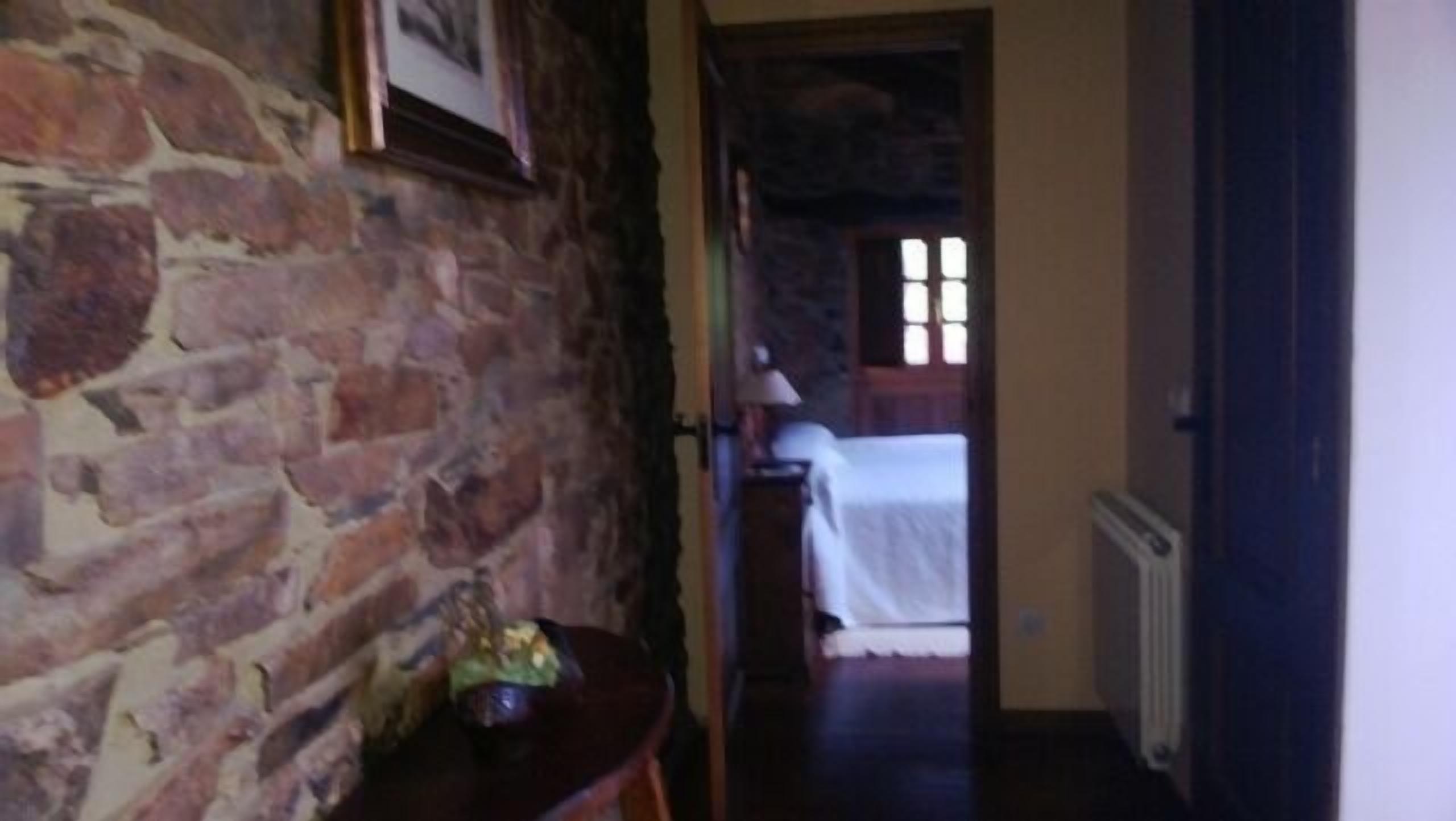 Un pasillo estrecho con una pared de piedra a un lado y una cama con colcha blanca a lo lejos.