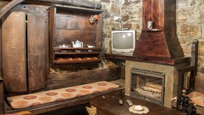 Een rustieke kamer met stenen muren, een houten bank, een open haard en een televisie.