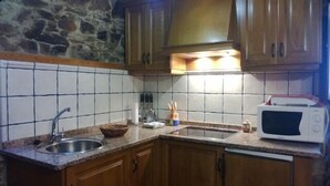 Een keuken met granieten aanrecht, een spoelbak, houten kastjes, een stenen muur en een magnetron.