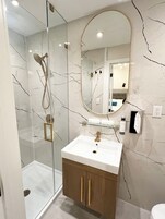 Een moderne badkamer met een douchecabine van glas, een witte wastafel met een gouden kraan en een houten kastje.