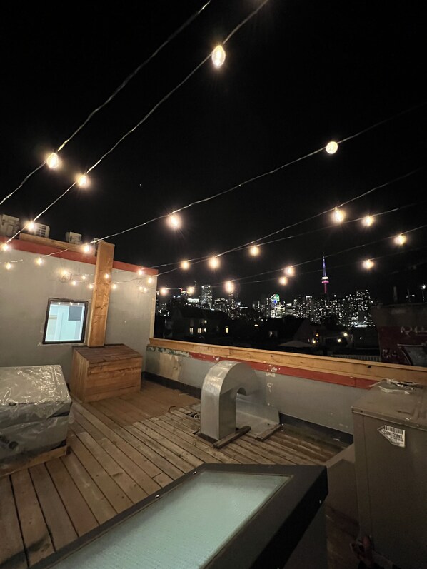 A rooftop terrace with string lights, a city view, and a wooden deck. - Toronto Rooms and Suites (Toronto)
