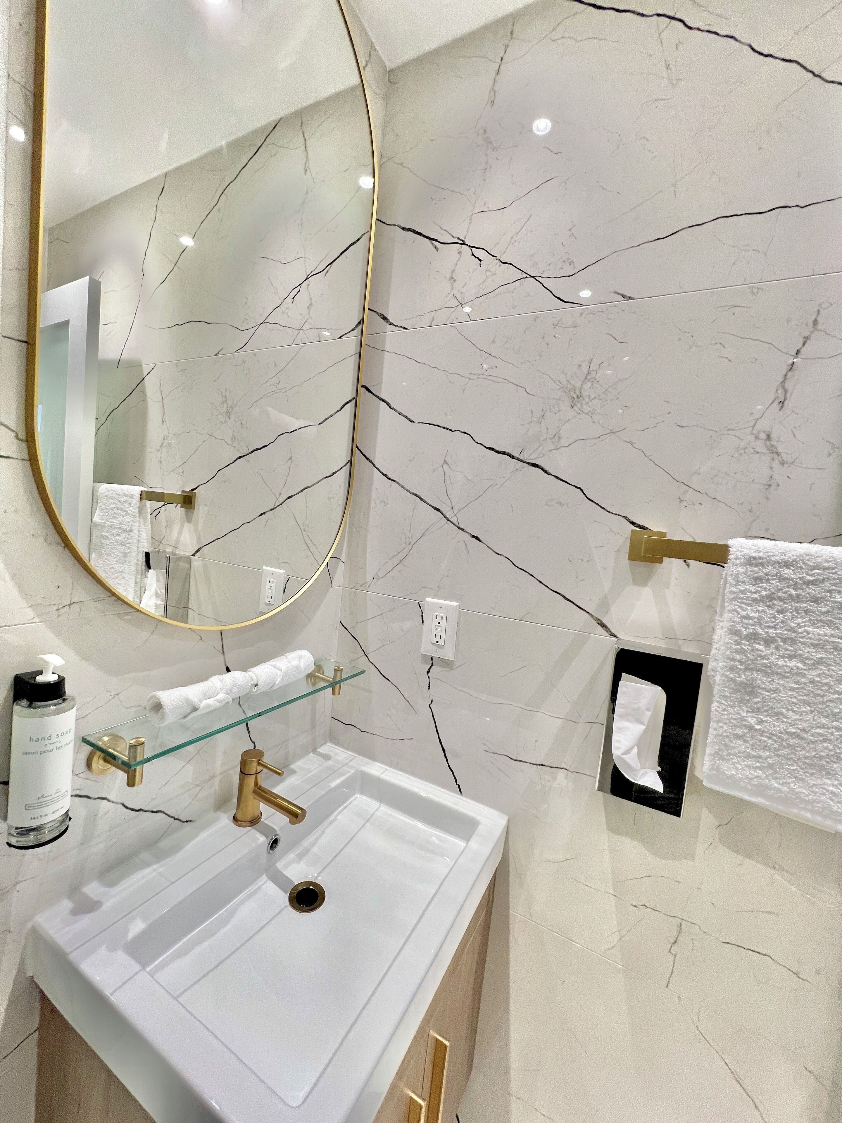 A bathroom with a white marble sink, gold fixtures, and a large mirror.