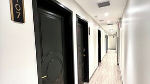 Un pasillo de hotel con puertas negras, un cartel con el número '107' y un piso de baldosas claras.