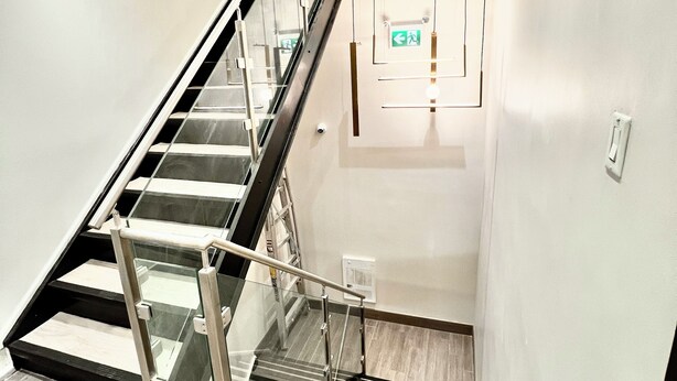 Una escalera moderna con barandillas de vidrio y pasamanos metálico, que conduce a un piso superior.