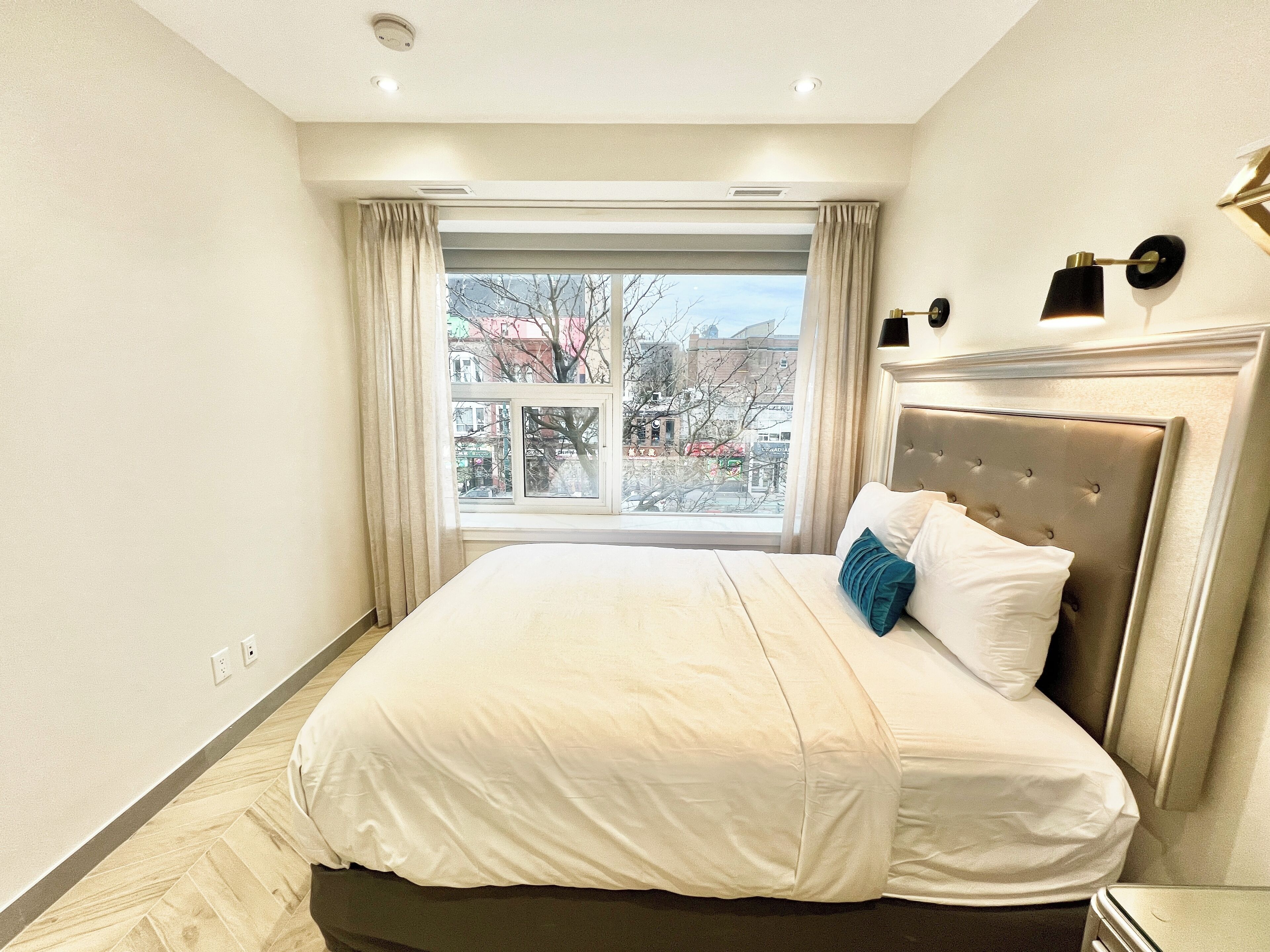 Un dormitorio moderno con una cama grande, una ventana con cortinas y vistas a la ciudad.
