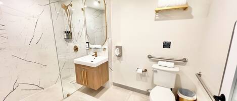 A modern bathroom with a glass shower enclosure, a wooden vanity, a toilet, and a handrail.