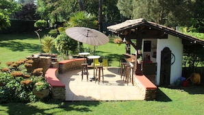 Zona de pati amb una zona de barbacoa, mobiliari d'exterior i un petit edifici amb una porta i una finestra.