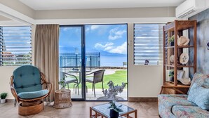 Een woonkamer met uitzicht op de oceaan, een rieten stoel, een bank en een glazen salontafel.