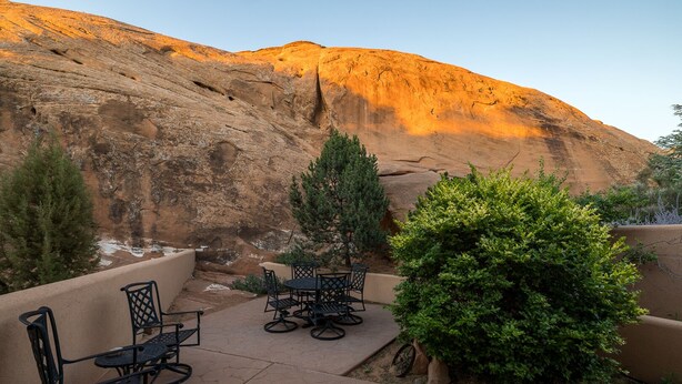 An outdoor patio with a table and chairs, surrounded by greenery and a mountainous backdrop.