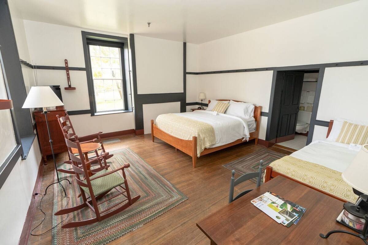 A bedroom with a wooden bed, a rocking chair, a desk, and a window.