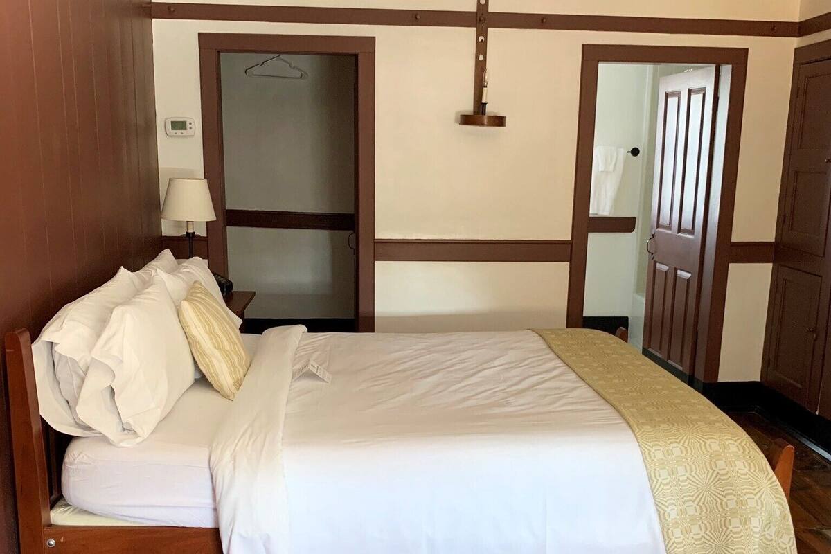 A neatly made bed with white linens, a wooden headboard, and a beige throw blanket.