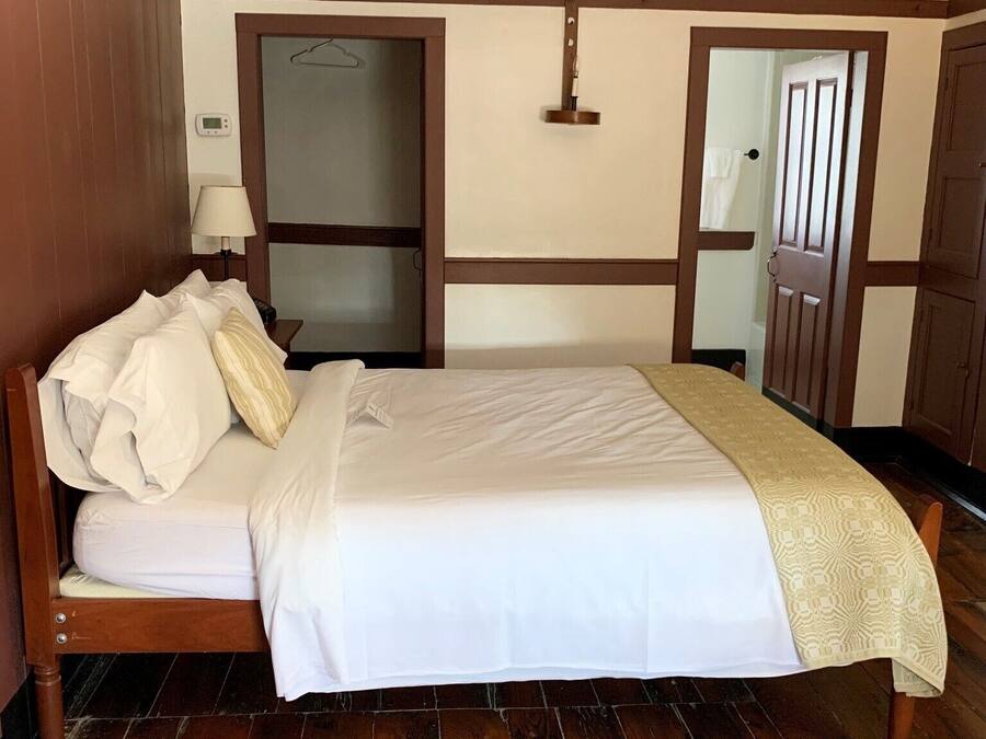 A neatly made bed with white linens, a wooden headboard, and a beige throw blanket.