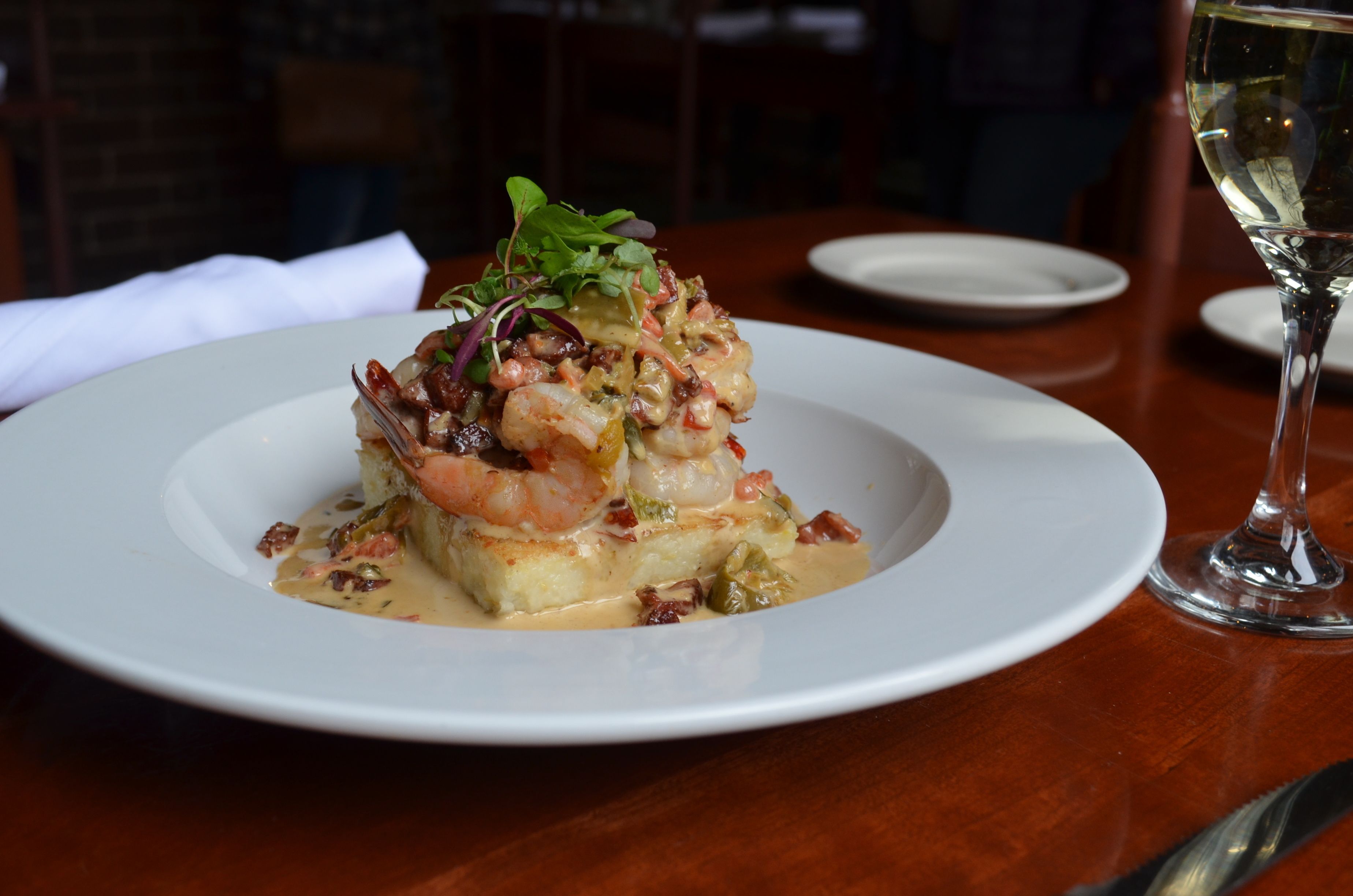 A plate of seafood dish with a glass of white wine on a wooden table.